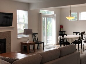 A living room with a fireplace, a sofa, a dining table with chairs, and a TV mounted on the wall. - Nightly or short term rental in Medford. (Medford)