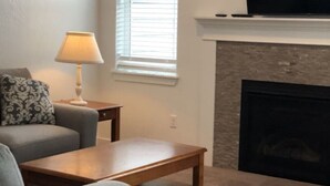 A living room with a sofa, a coffee table, a lamp, a fireplace, and a television. - Nightly or short term rental in Medford. (Medford)