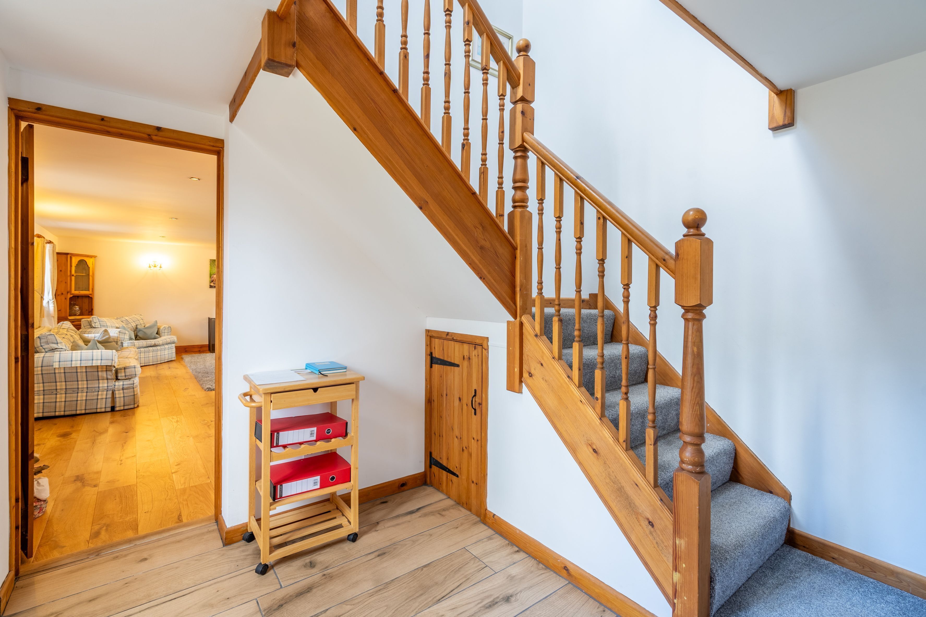 Eine Holztreppe mit Handlauf und Teppichstufen führt zu einer oberen Etage. Ein hölzerner Wagen mit roten Kisten steht in der Nähe der Treppe.