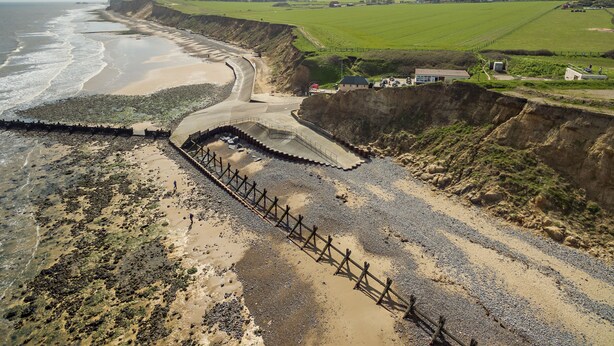 Paisaje costero con playa, acantilado y una zona delimitada por una valla.