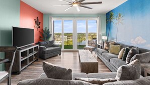 A living room with a TV, sofas, a coffee table, and a ceiling fan. - Palm Tree Paradise – Free Beach Chairs & Umbrella, 5 Pools, Beach Access | Laketown Wharf 1531 (Panama City Beach)