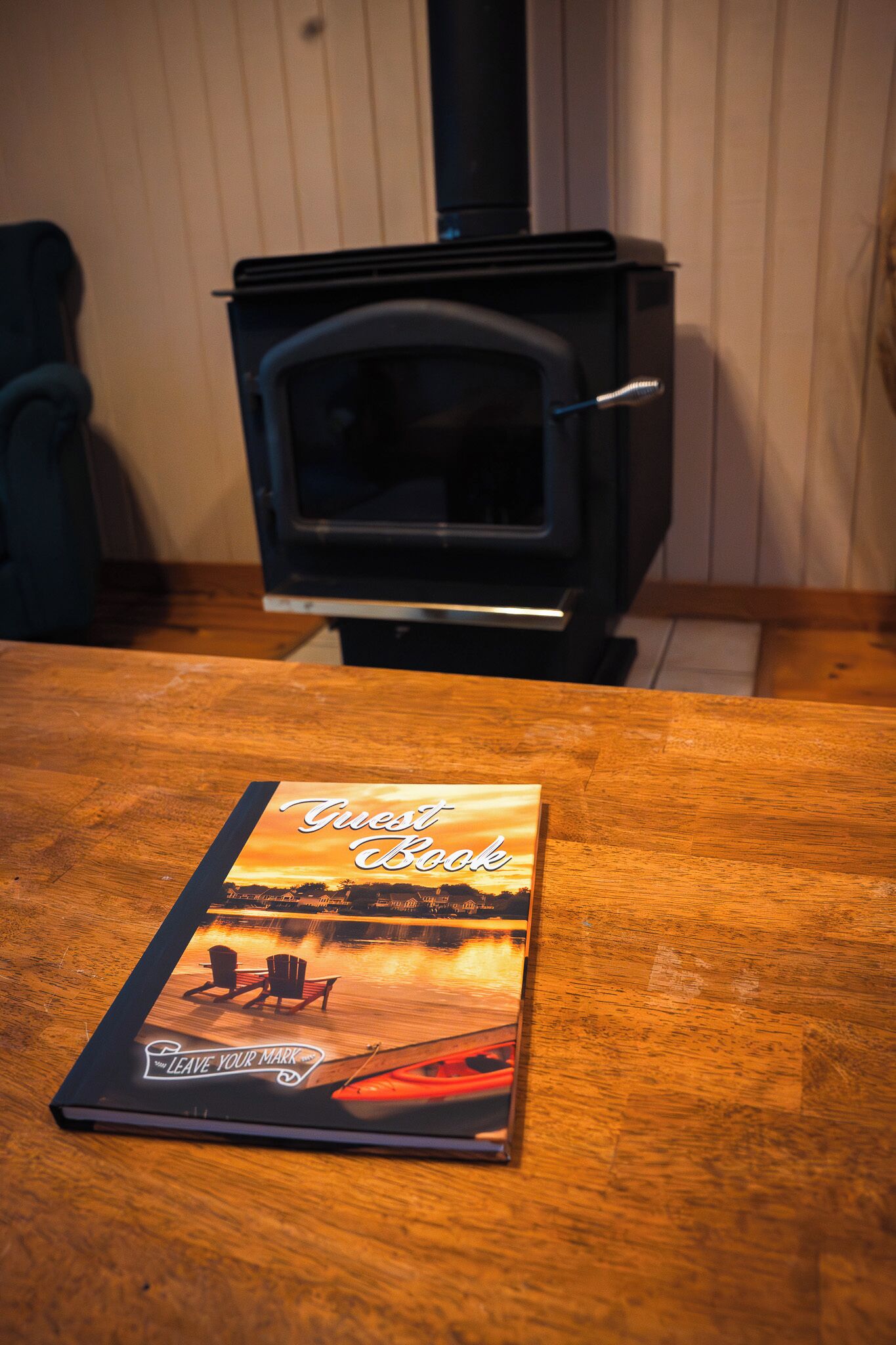 Un libro con el título 'Guest Book' sobre una mesa de madera, con una estufa de leña al fondo.