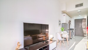 Un salon moderne doté d’un grand téléviseur à écran plat, d’un coin repas avec une petite table et des chaises, et d’une cuisine en arrière-plan.