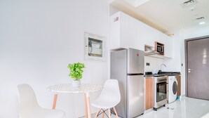 Une cuisine moderne équipée d’un réfrigérateur, d’un four, d’un four à micro-ondes et d’un lave-linge. On y trouve une petite table à manger avec deux chaises et une plante en pot.