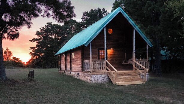 Une cabane en bois avec des fondations en pierre, une véranda dotée de balustrades en bois et un toit en métal.