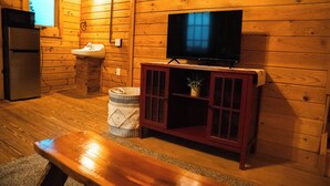 L’intérieur d’une cabane en bois, avec un téléviseur posé sur un meuble, un réfrigérateur, un évier et un banc.