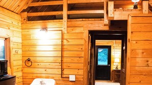 L’intérieur d’une cabane en bois comprend un coin cuisine, un évier, une échelle en bois et une porte donnant sur une autre pièce.