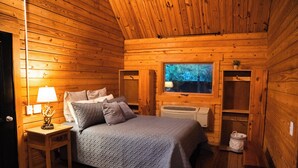 Une chambre confortable dans un chalet en bois, avec un lit, une table de chevet, une lampe et une fenêtre donnant sur la forêt.