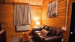 Une pièce chaleureuse avec des murs en bois, un canapé en cuir, une petite table en bois et une lampe.