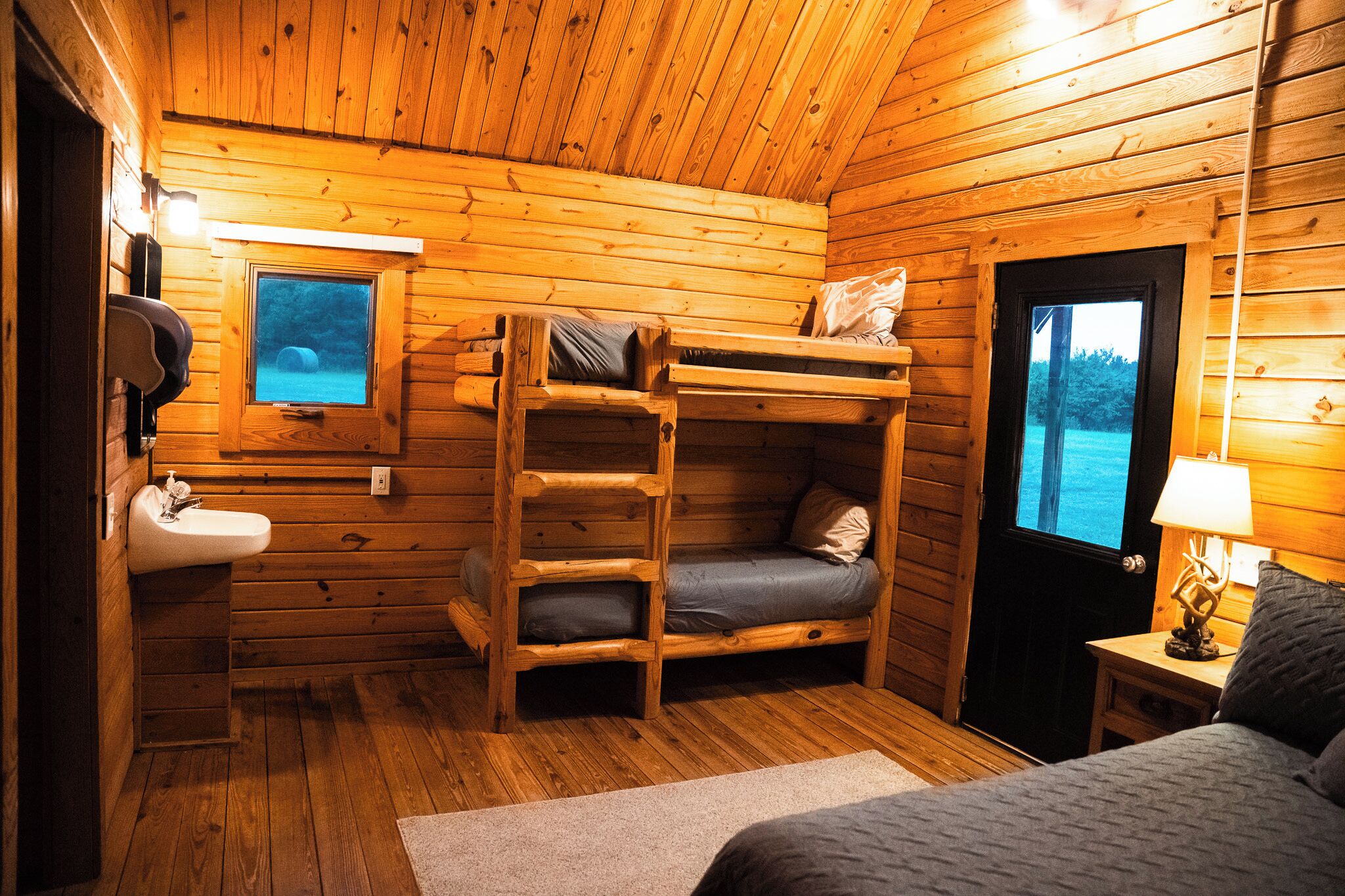 A cabin with bunk beds, a sink, a window with a view, and a door.