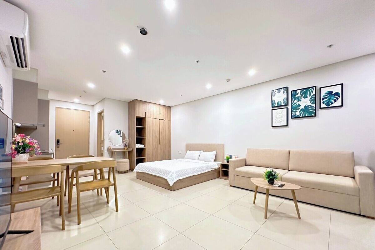 A modern, well-lit bedroom with a bed, a sofa, a coffee table, and a dining area with chairs and a table.