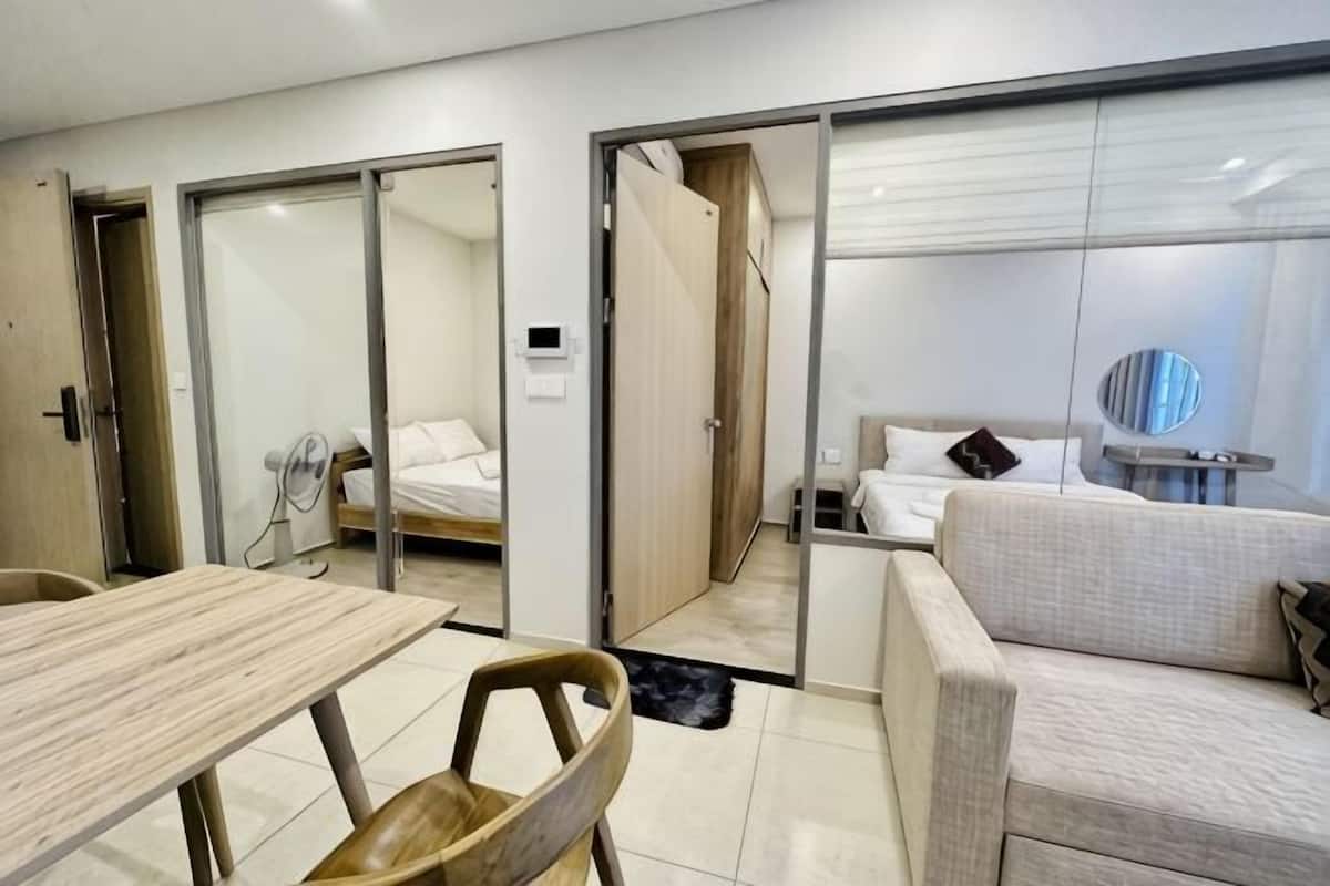 A modern hotel room with a wooden table, a sofa, a bed, and a glass partition.