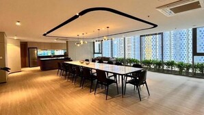 Un comedor moderno con una mesa larga y sillas, una cocina al fondo, y ventanas grandes con vistas.