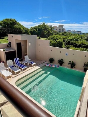 A rooftop pool with lounge chairs and potted plants.