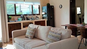 Ein modernes Wohnzimmer mit einem beigen Sofa, einem Holztisch und einem Essbereich mit Tisch und Stühlen.