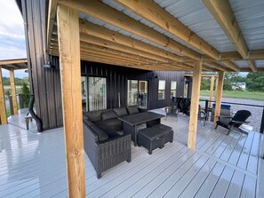Un espacio al aire libre techado con sofá y sillones, una mesa y una parrilla.