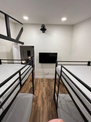Habitación tipo dormitorio con literas, un televisor de pantalla plana en la pared y piso de madera.