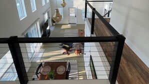 A spacious interior with a high ceiling, multiple windows, and a staircase leading to an upper level.