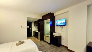 Habitación de hotel con dos camas, un televisor montado en la pared, un escritorio con computadora y una puerta corrediza que da al baño.