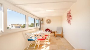 A sunlit room with a table and chairs, a view through large windows, and a decorative wall piece. - One haven with stunning views (Alcabideche)