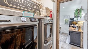 A laundry area with two stacked washers and dryers, a sign above them, and a small kitchenette in the background. - Welcoming Guest Suite in Snohomish (Snohomish)