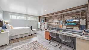 A modern bedroom with a bed, a desk, and a sofa. There is a window with blinds, a bookshelf, and a TV on the wall. - Welcoming Guest Suite in Snohomish (Snohomish)