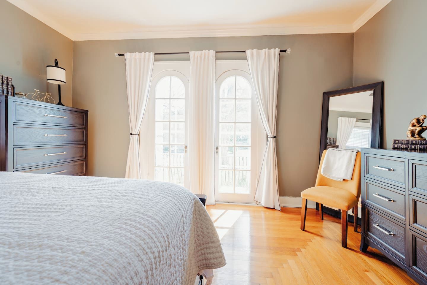 Een slaapkamer met een bed, een kaptafel, een stoel en een groot raam met gordijnen.