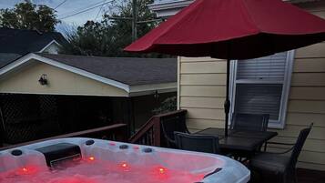 Un jacuzzi con un paraguas rojo, una terraza de madera y un porche cubierto.