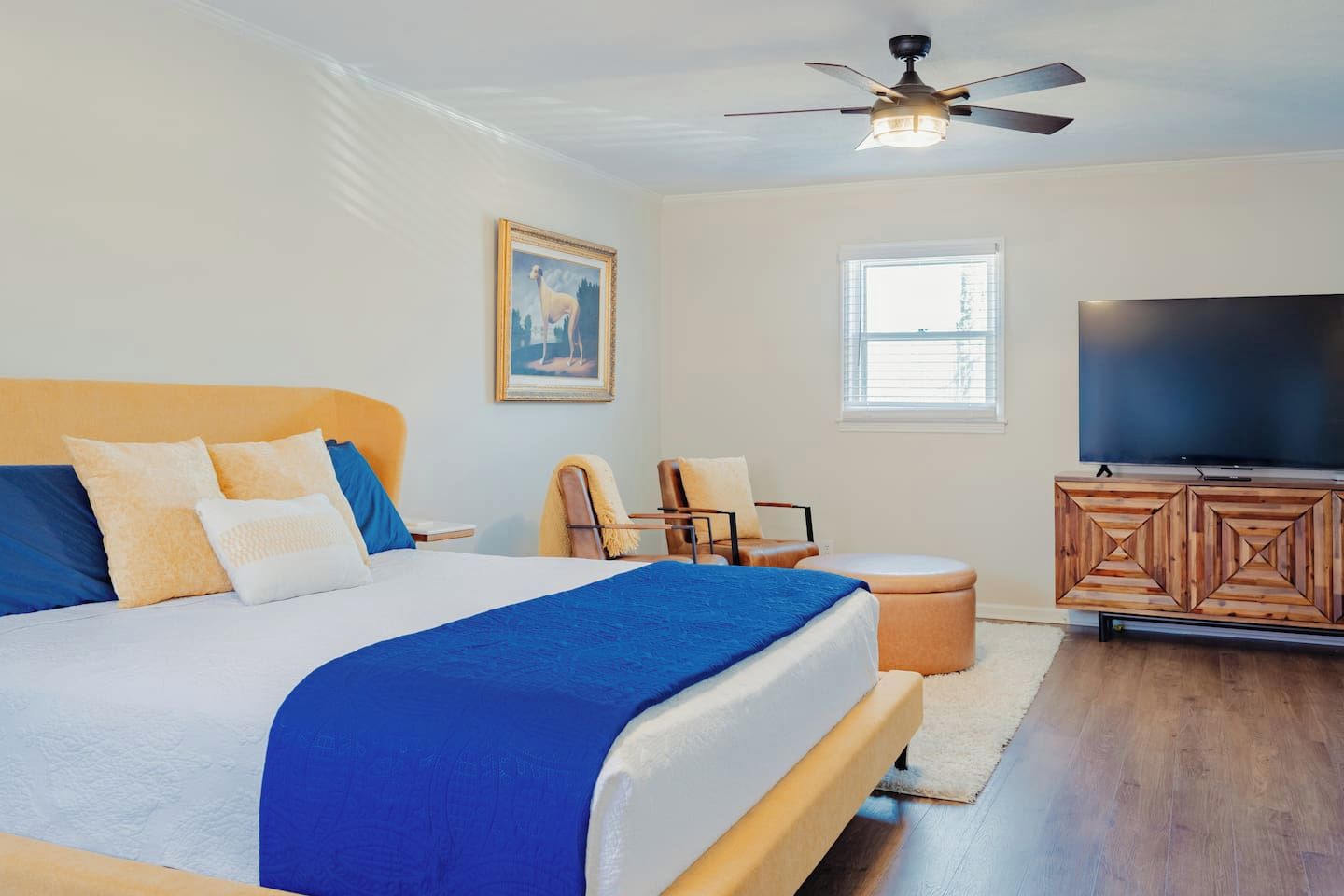 A bedroom with a bed, a television, a ceiling fan, and a window.