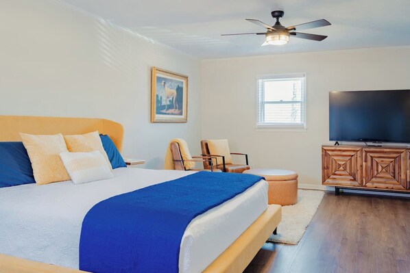 A bedroom with a bed, a television, a ceiling fan, and a window.