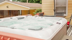 Un jacuzzi al aire libre con un paraguas rojo, una terraza de madera y una casa amarilla al fondo.