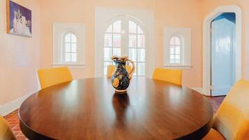 A round table with a pitcher in the center, surrounded by yellow chairs, in a room with arched windows and a chandelier.