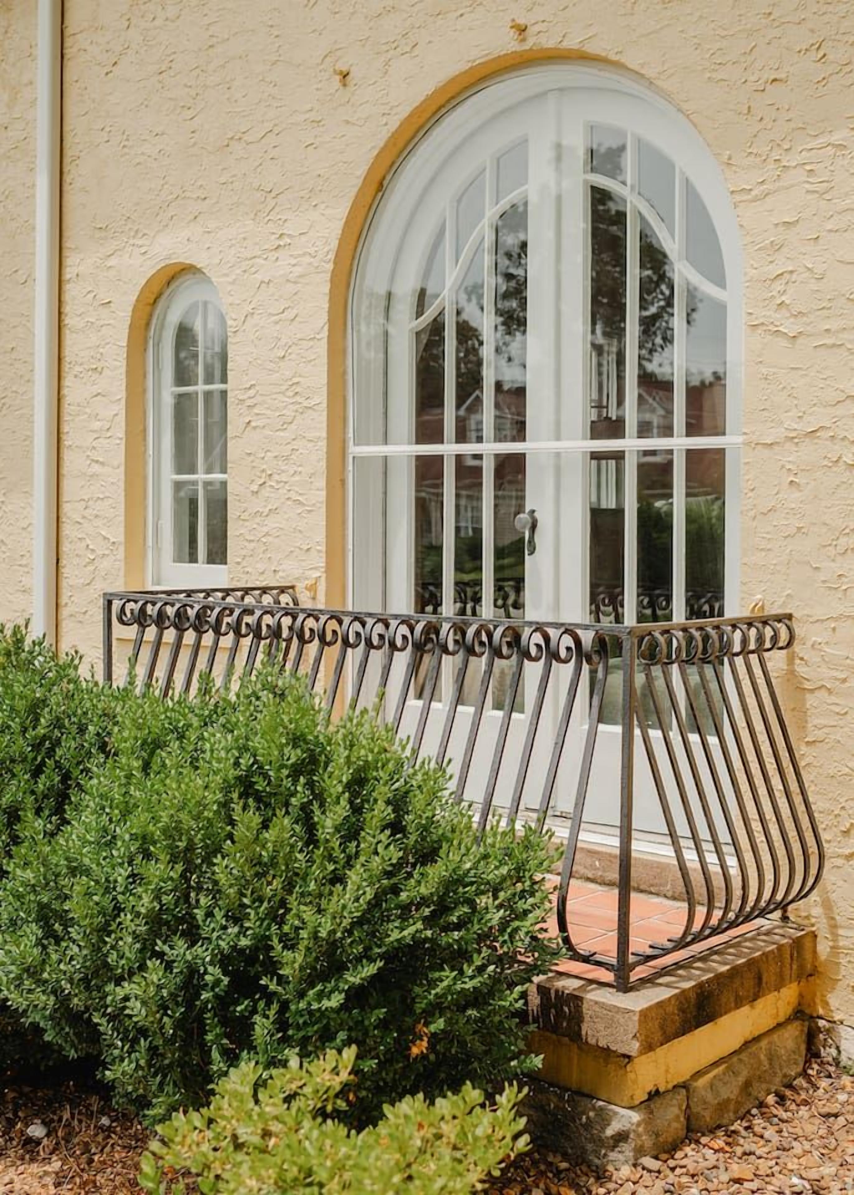 A building with a textured facade, a metal railing, and a window with a white frame.