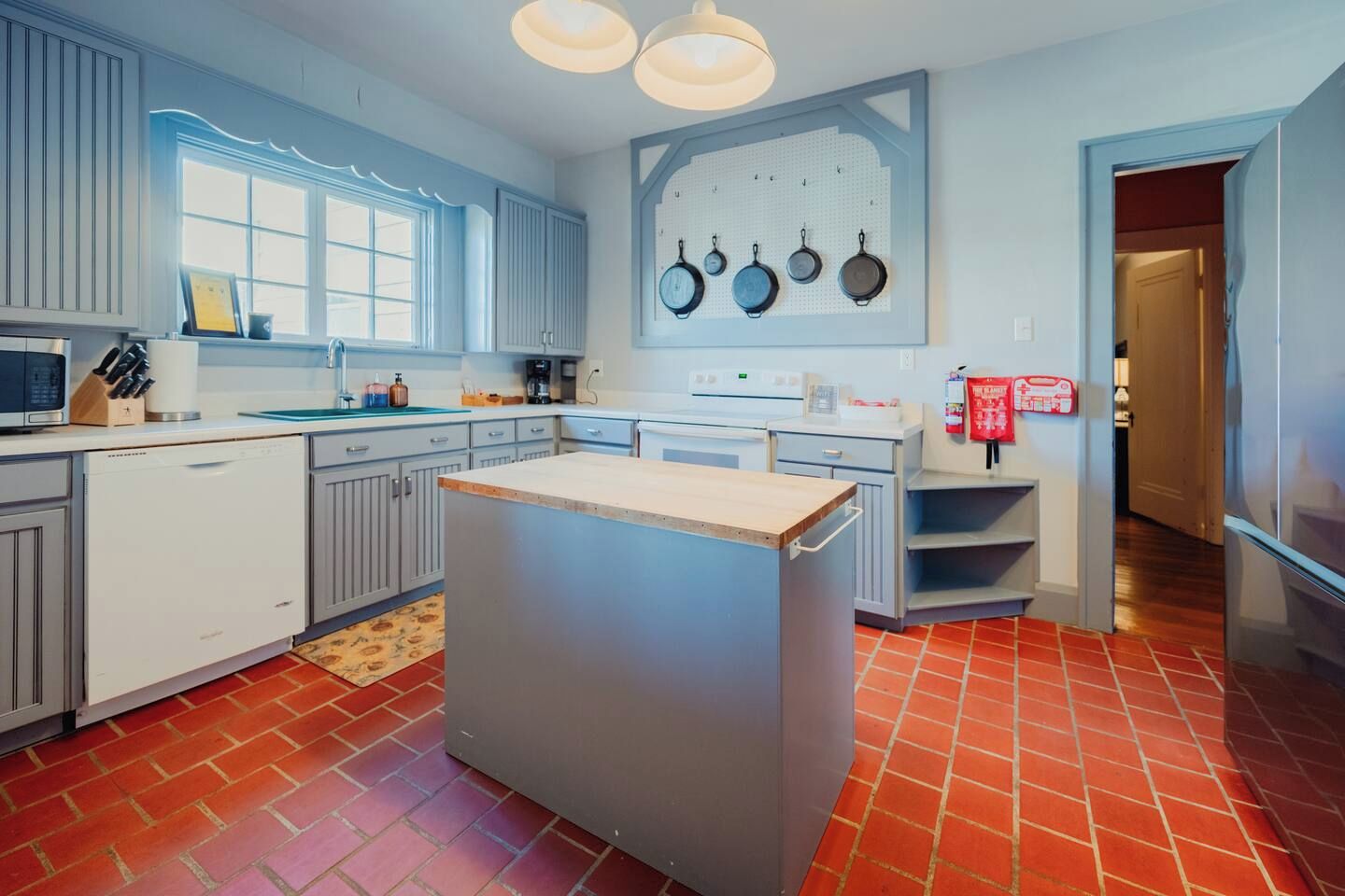 Une cuisine moderne dotée d’un îlot central, de meubles blancs et d’un sol carrelé de carreaux rouges.