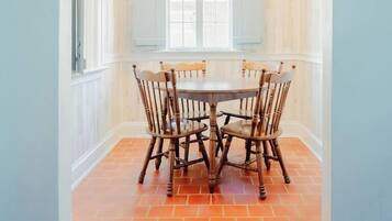 A dining area with a round table and chairs, an arched doorway, and a window with blinds.