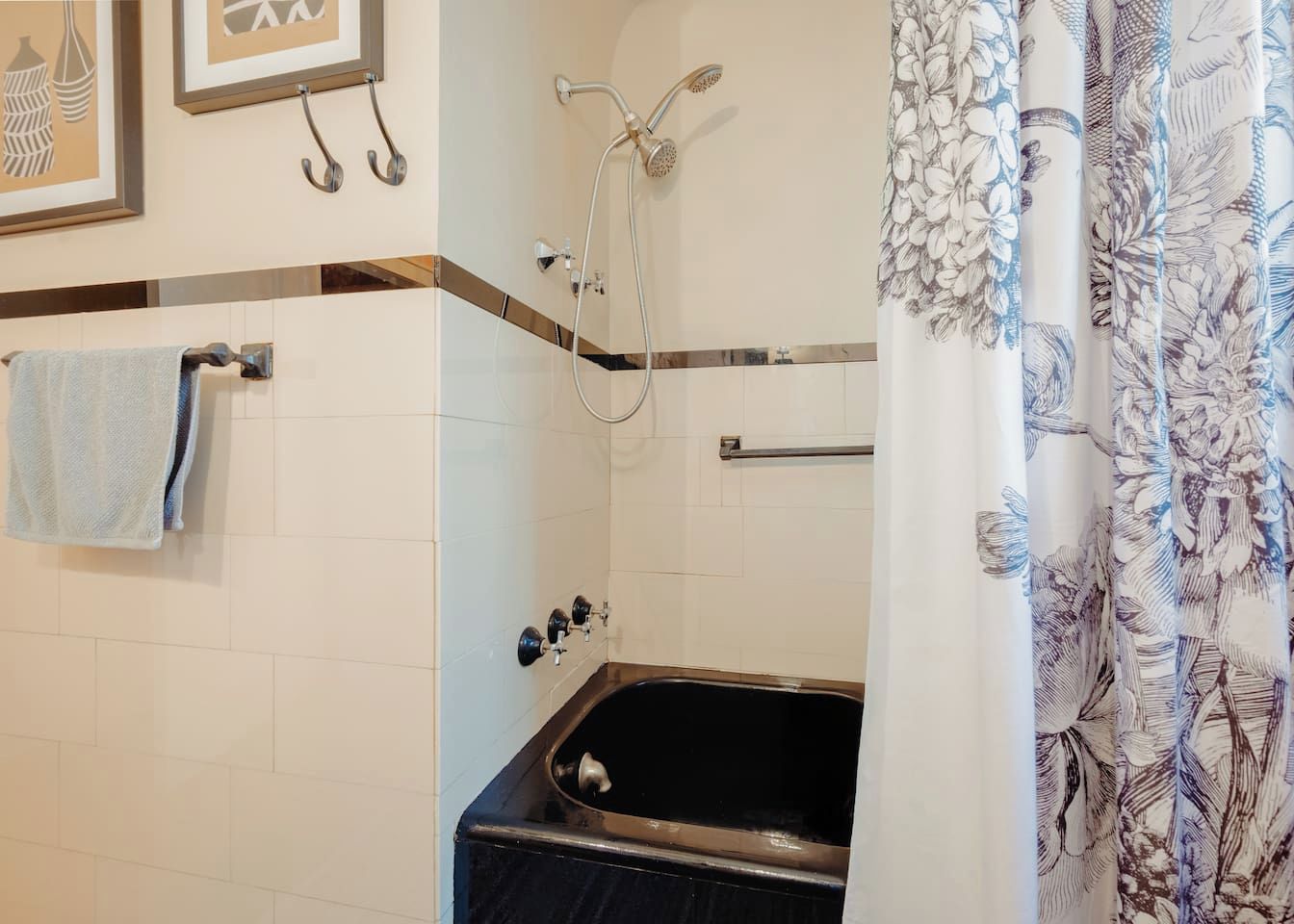 Een badkamer met een bad, douche, handdoekhouder en een gordijn met een bloemenmotief.