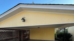Un área de estacionamiento techada con piso de concreto, cerca metálica y un edificio de fachada amarilla.