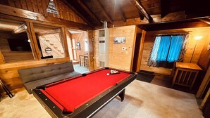 Une table de billard dans une pièce aux murs en bois et où se trouve un canapé.
