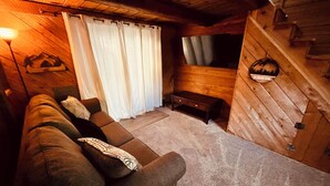 Une chambre confortable, aménagée dans le style d’un chalet, avec un canapé, des rideaux, une petite table et un téléviseur fixé au mur.