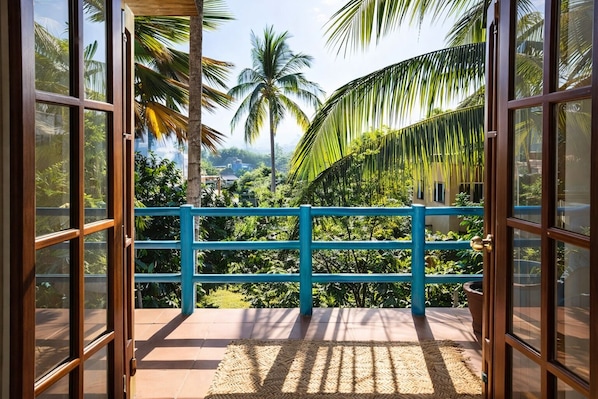 A balcony with a blue railing, a woven mat, and a view of tropical vegetation and palm trees.