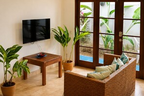 Un salon avec un téléviseur, une table, un canapé en osier et des plantes en pot.