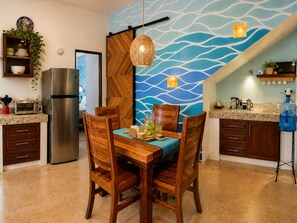 A modern kitchen with a dining area, featuring a large water-themed wall, a stainless steel refrigerator, and wooden chairs.