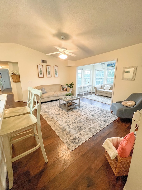 A spacious living room with a ceiling fan, a dining area with a wooden chair, and a cozy seating area with a wicker chair.