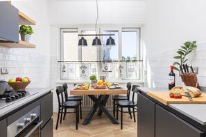 Eine moderne Küche mit Esstisch, Stühlen und einer Arbeitsplatte, auf der ein Brotmesser und eine Flasche liegen.