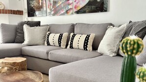 Una sala moderna con un sofá seccional gris, una mesa de centro redonda de madera y una planta de cactus.