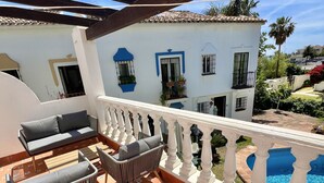 Una terraza con piscina, mobiliario exterior y un edificio blanco con marcos azules en las ventanas.