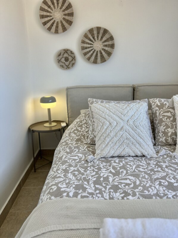 Een slaapkamer met een bed, kussens, een nachtkastje en wanddecoratie.