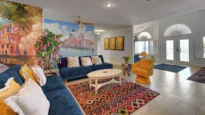 Un salón espacioso con un cuadro grande de Venecia, un conjunto de sofá azul, una mesa de centro y una alfombra colorida.