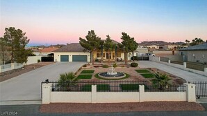 Una propiedad residencial con entrada de vehículos, garaje, jardín delantero ajardinado con una fuente y cielo despejado.
