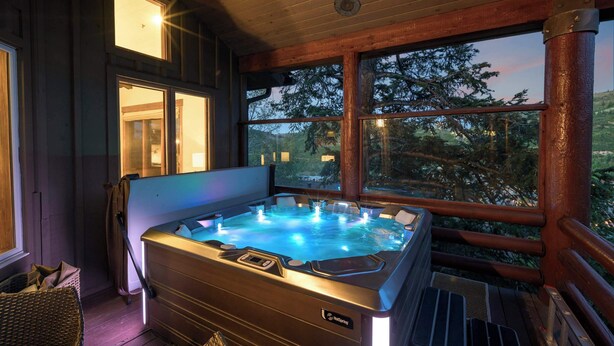 Un bain à remous avec une terrasse en bois, de grandes fenêtres et une vue sur les arbres.